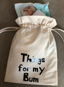 A canvas drawstring bag with Things for my bum printed on the front and nappy and wipes poking out of the top.