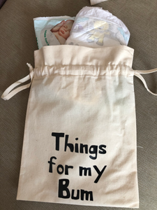 A canvas drawstring bag with Things for my bum printed on the front and nappy and wipes poking out of the top.