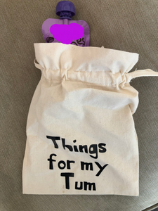 A canvas drawstring bag with Things for my tum printed on the front and a baby food pouch poking out of the top.